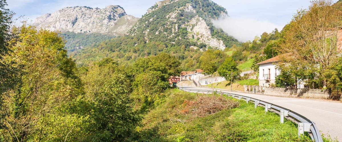A winding road through a mountainous area with lush greenery and a prominent rocky mountain in the background.