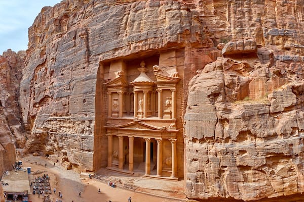 Une façade taillĂ©e dans la roche, ornĂ©e de colonnes et dâune arche centrale, le tout entourĂ© dâescarpements rocheux.