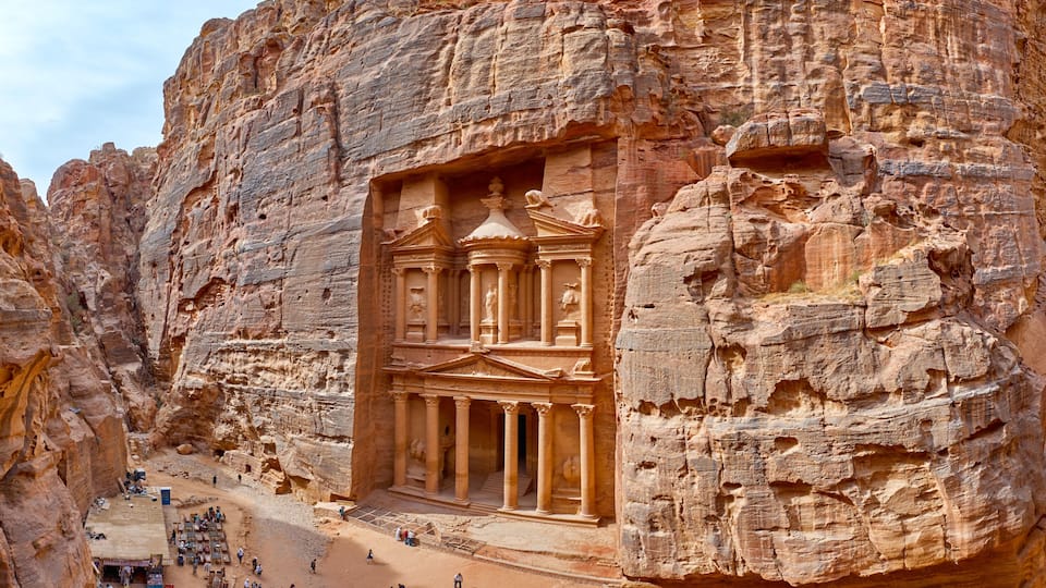 A rock-cut facade with columns and a central archway, surrounded by rugged cliffs.