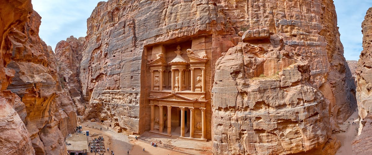 A rock-cut facade with columns and a central archway, surrounded by rugged cliffs.