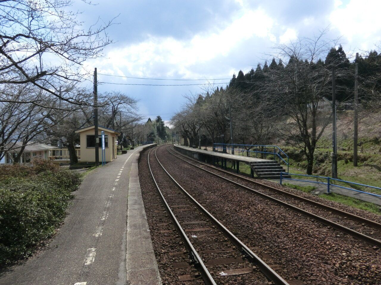 A railway track with a platform, a small building, and trees in the background.