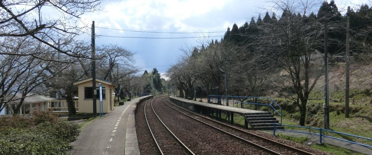 A railway track with a platform, a small building, and trees in the background.