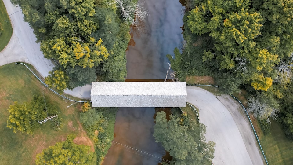 An aerial view of a building surrounded by a river, roads, and dense greenery.