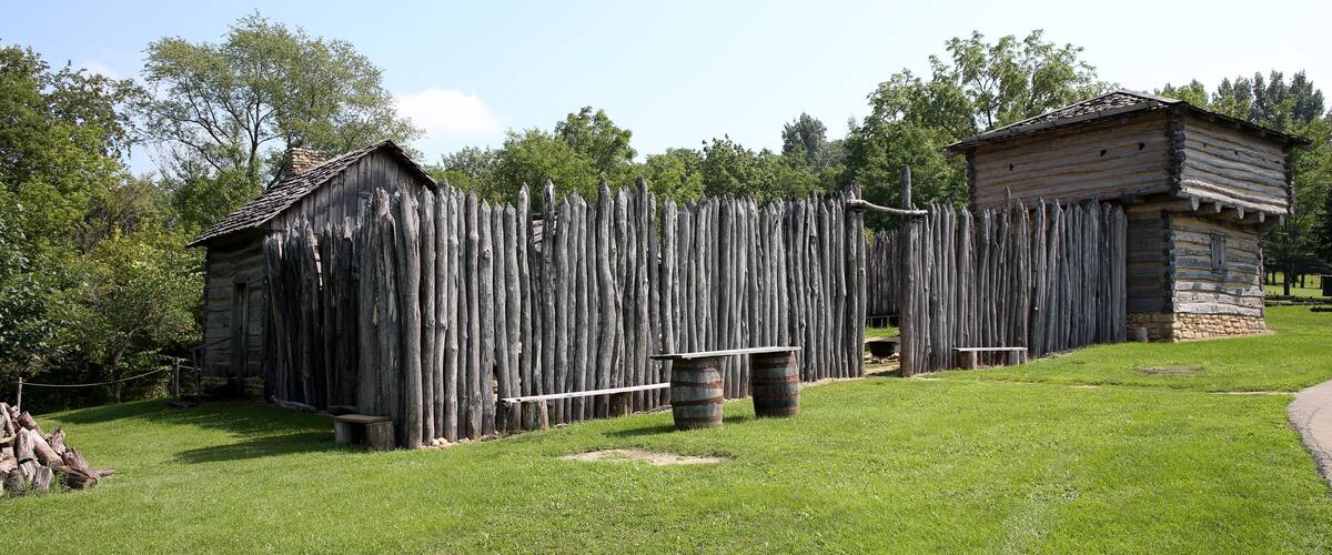 A rustic wooden fence, a stone building, and a grassy field.