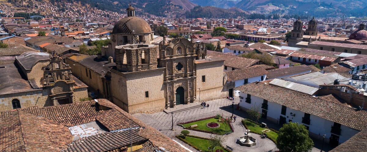 A historic town with a prominent church, terracotta-roofed buildings, and a mountainous backdrop.