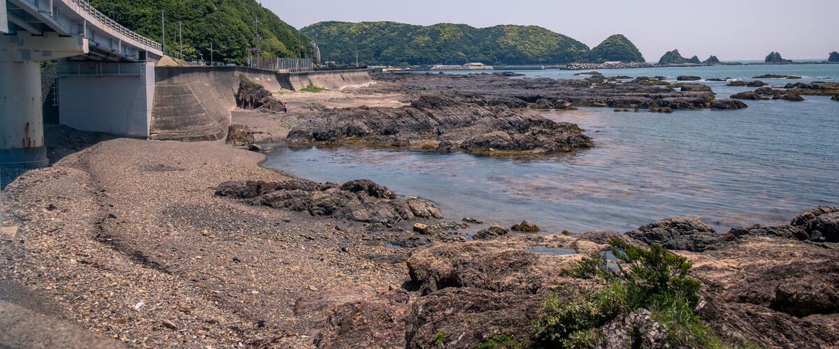 A coastal landscape with rocky shores, a bridge, and lush green hills in the background.