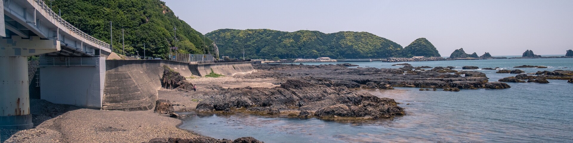 A coastal landscape with rocky shores, a bridge, and lush green hills in the background.