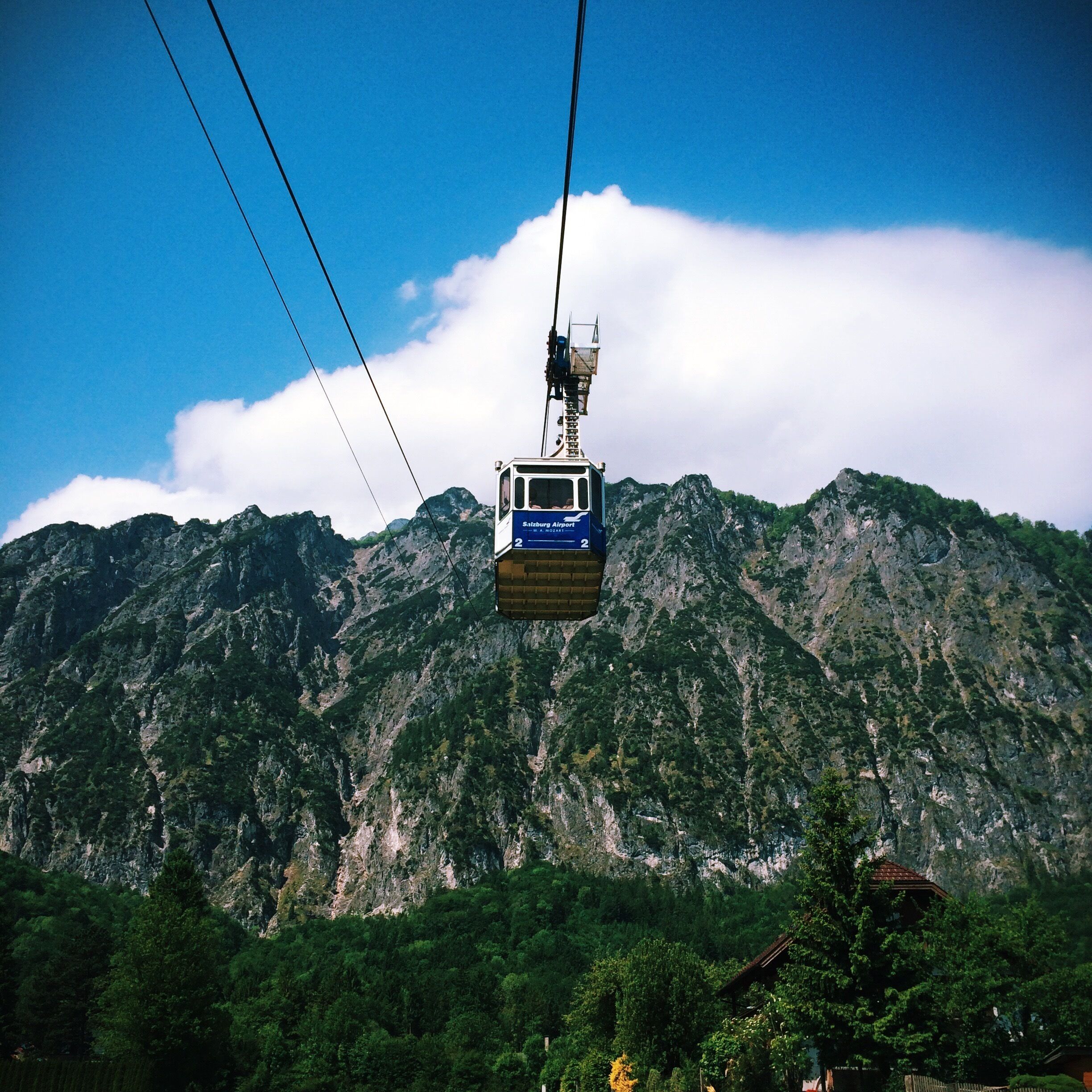 A cable car suspended over a mountainous landscape with lush greenery and rocky cliffs.