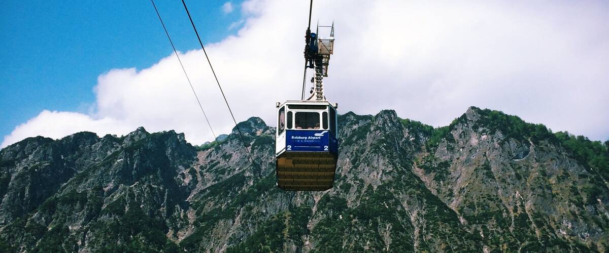 A cable car suspended over a mountainous landscape with lush greenery and rocky cliffs.