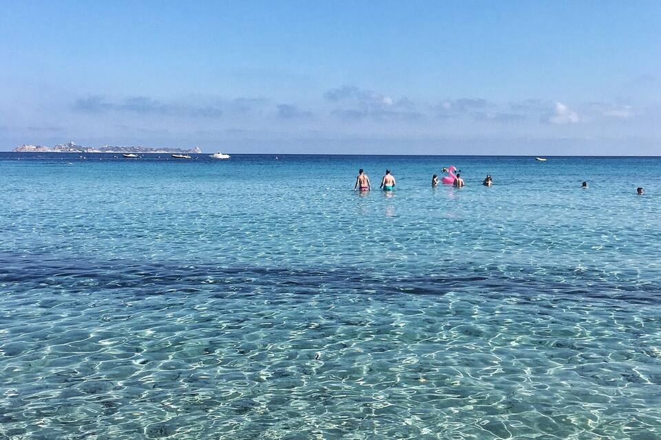 Krystalklart turkis vand, enkelte badegæster og fjerne både.