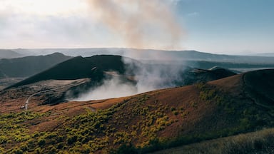 Un paisaje montañoso con una carretera serpenteando y humo elevándose desde las colinas.