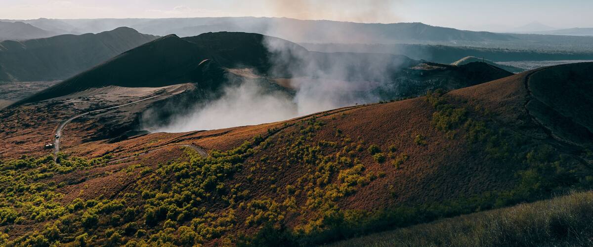 A hilly landscape with a road winding through it and smoke rising from the hills.