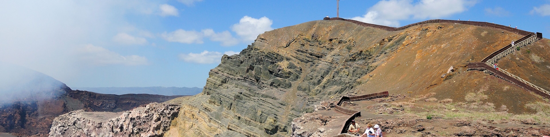 Una cruz en la cima de una colina, terreno rocoso y un camino pavimentado.