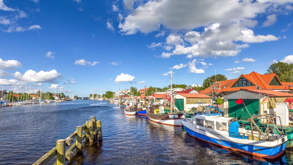 A harbor with boats, a wooden pier, and buildings with red roofs.