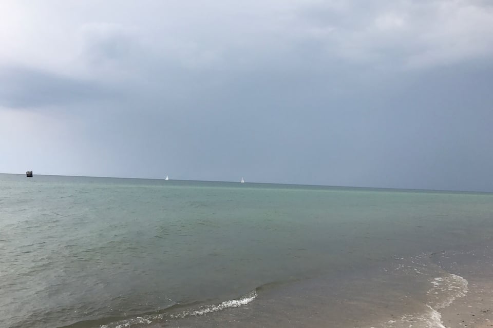 A beach with calm waters, a distant boat, and a cloudy sky.