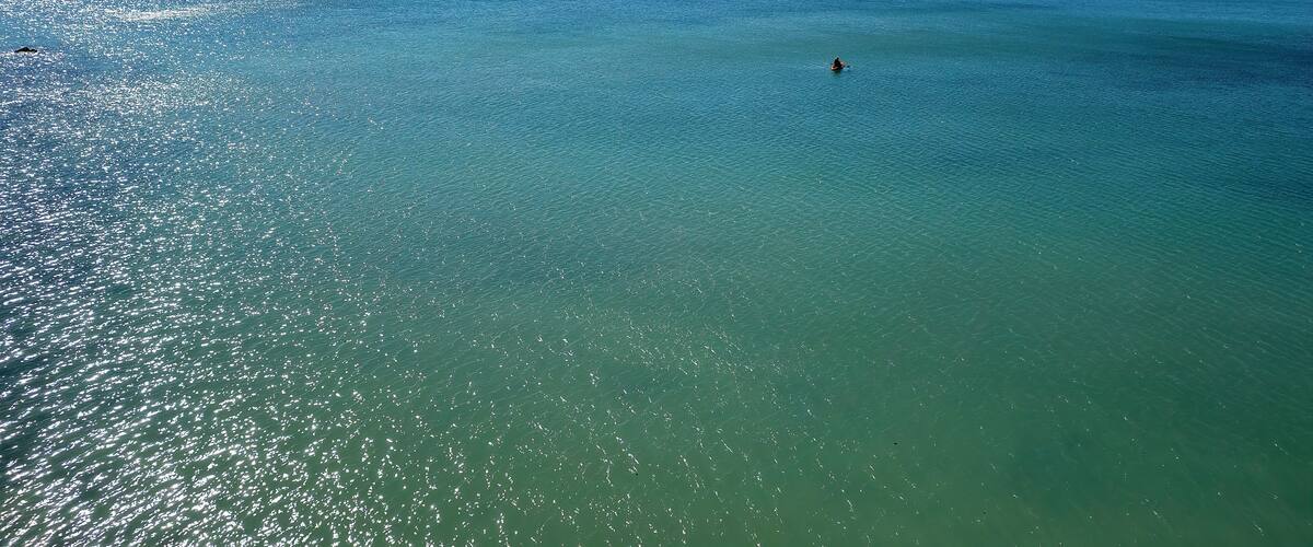 A clear turquoise sea with a person paddling, distant islands, and a clear sky.