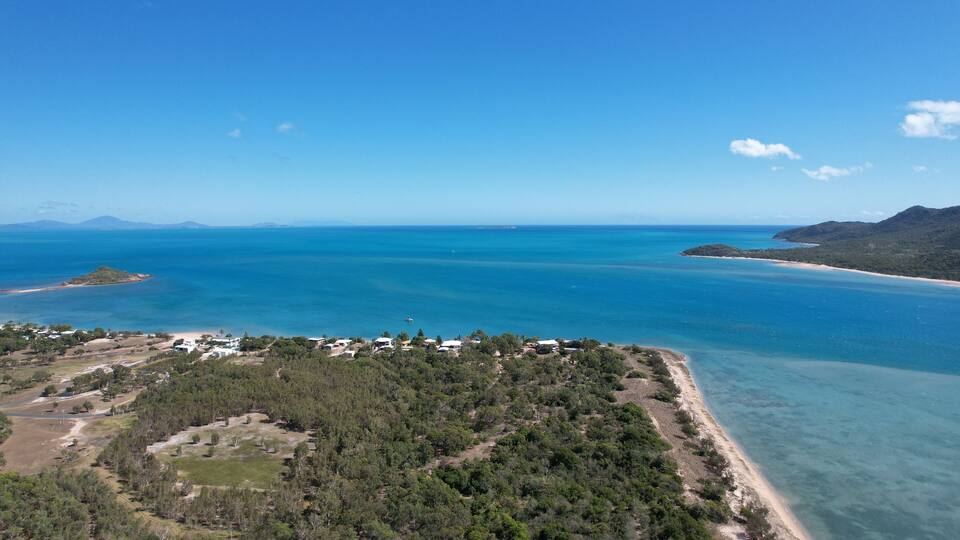 A coastal landscape with a beach, clear blue waters, and a forested area.