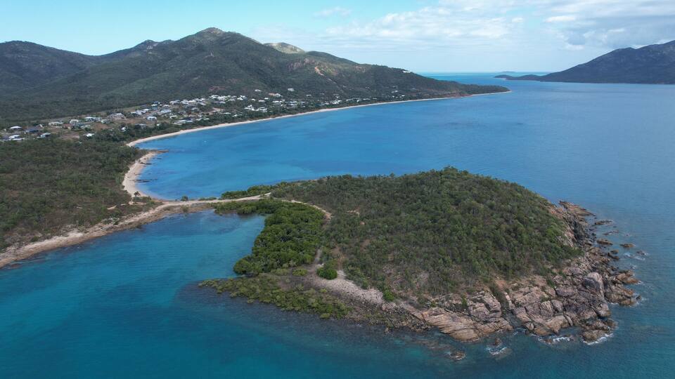 A coastal landscape with a beach, a small island, and mountains in the background.