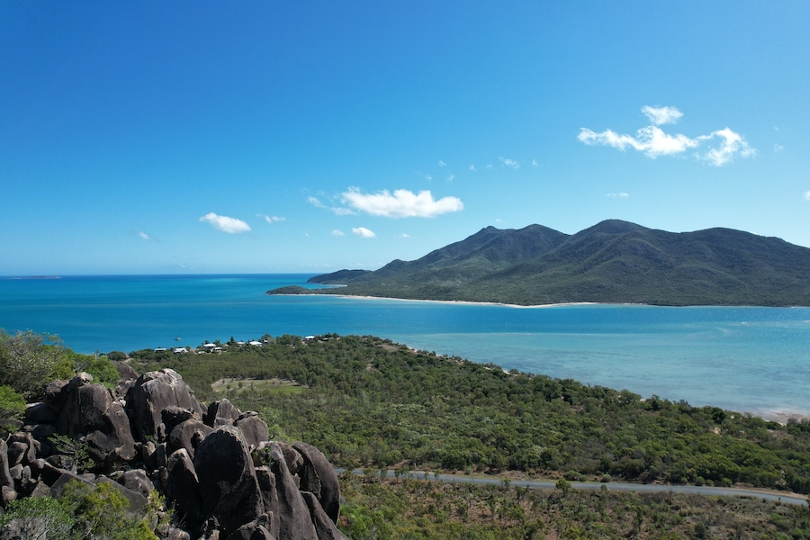 A coastal landscape with a mountain range, a beach, and a road leading to the coast.