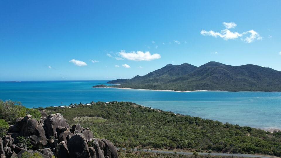 A coastal landscape with a mountain range, a beach, and a road leading to the coast.