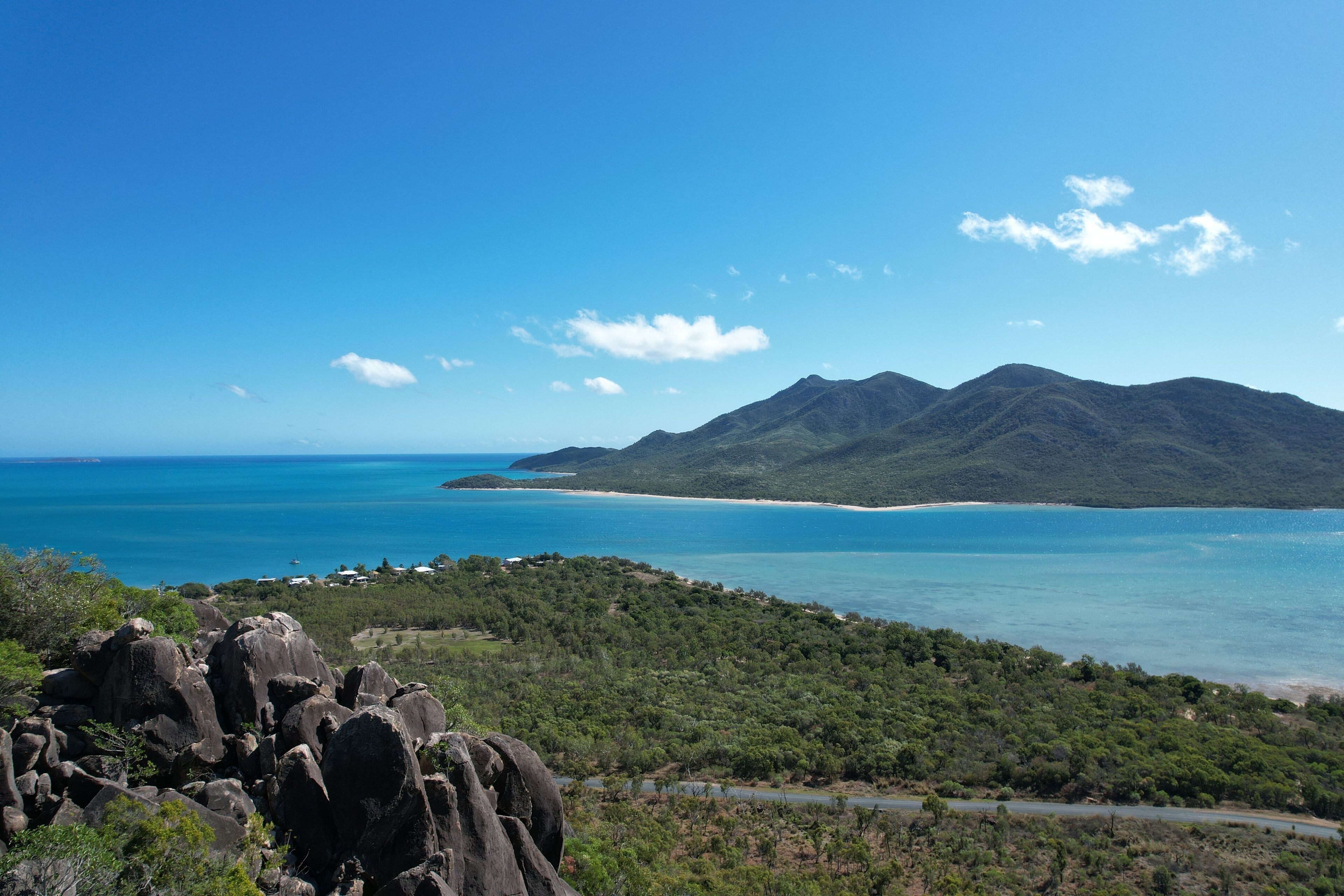 A coastal landscape with a mountain range, a beach, and a road leading to the coast.