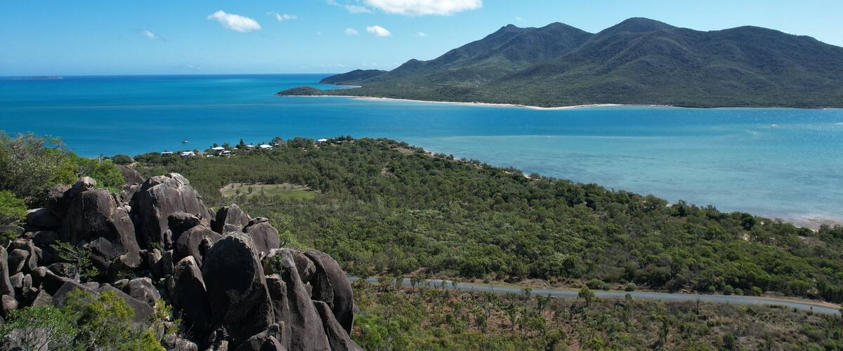 A coastal landscape with a mountain range, a beach, and a road leading to the coast.