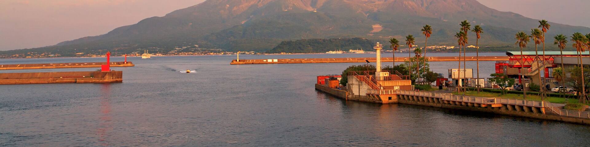 A coastal scene with a mountain in the background, a harbor with boats, and a red lighthouse.