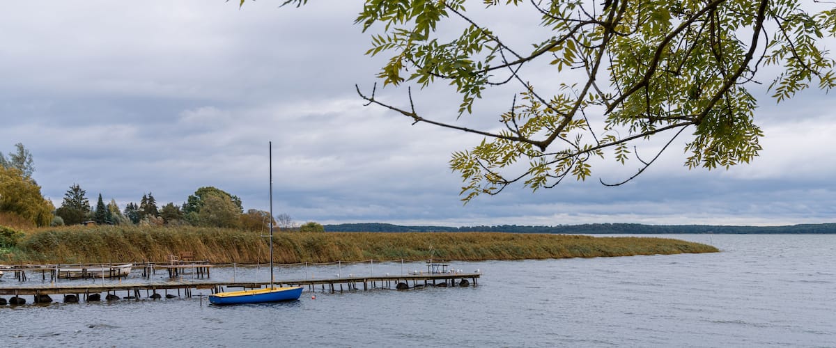 A calm lake with a wooden dock and a blue boat anchored near the shore.