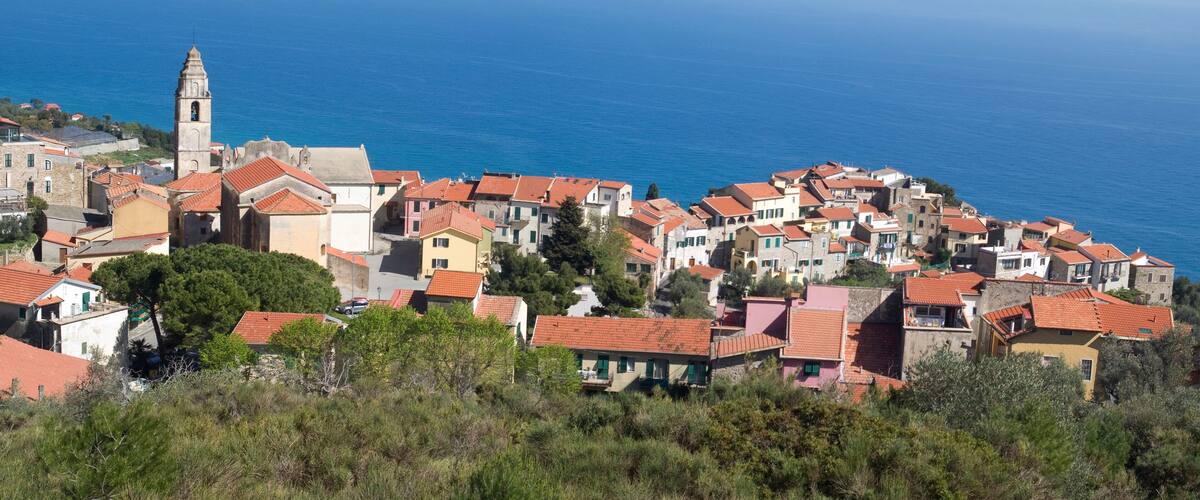 A coastal village with terracotta-roofed houses, a prominent church tower, and the sea in the background.