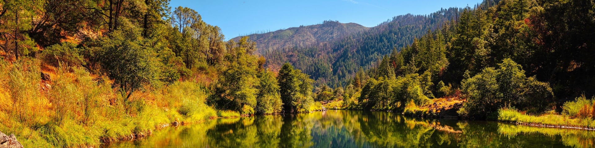 Autumn foliage and tranquil water reflections over the rocky creek on Trinity River near Del Loma, Northern California