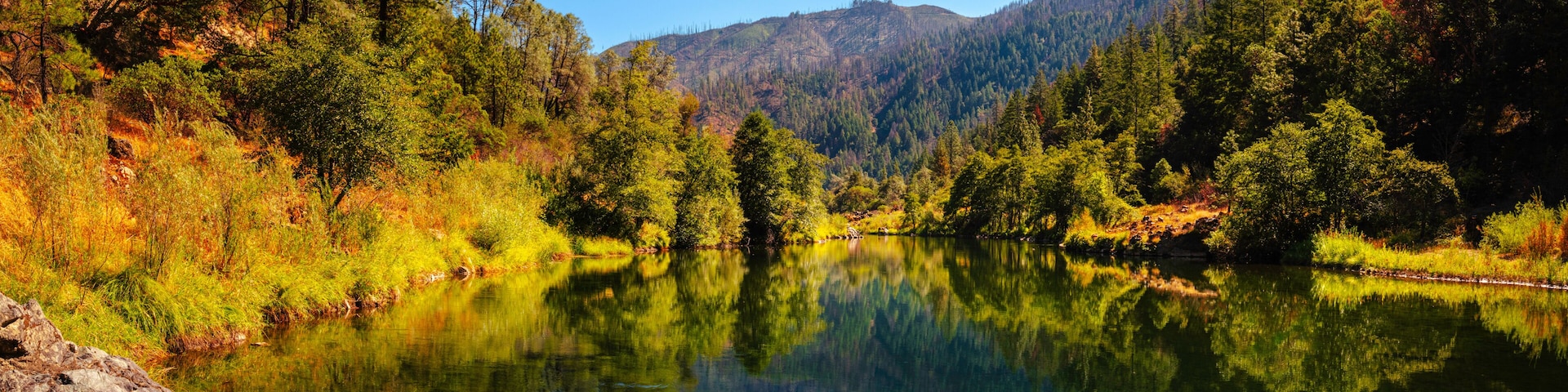 Autumn foliage and tranquil water reflections over the rocky creek on Trinity River near Del Loma, Northern California