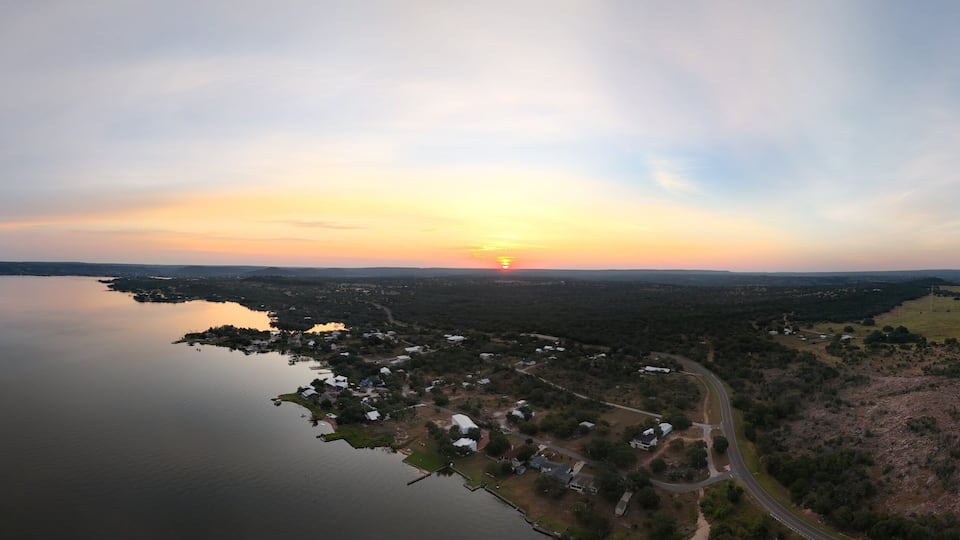 A sunset over a coastal town with a lake, surrounded by forested hills.