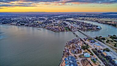 High dynamic range aerial sunset photo of lake, bridge and town under cloudy skies with vivid sunset. Contrasting warm and cool tones.