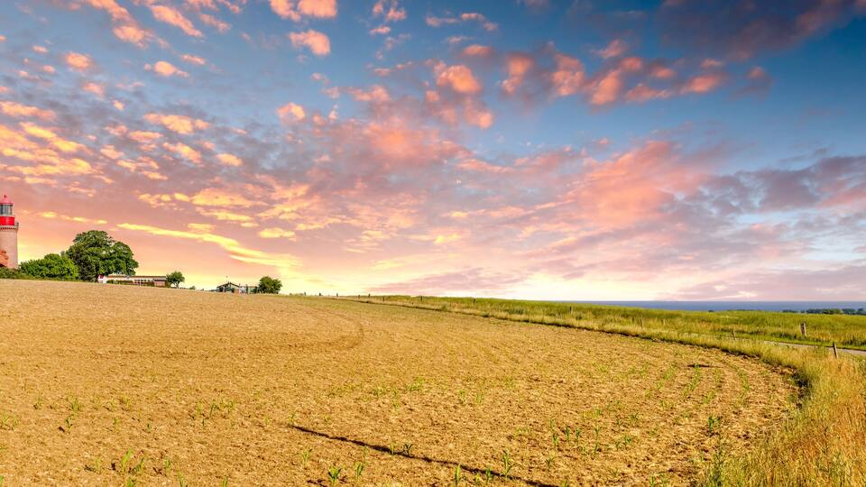 A sunset over a field with a red tower and a paved path.