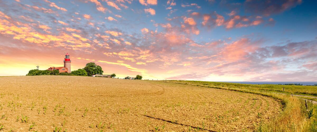 A sunset over a field with a red tower and a paved path.