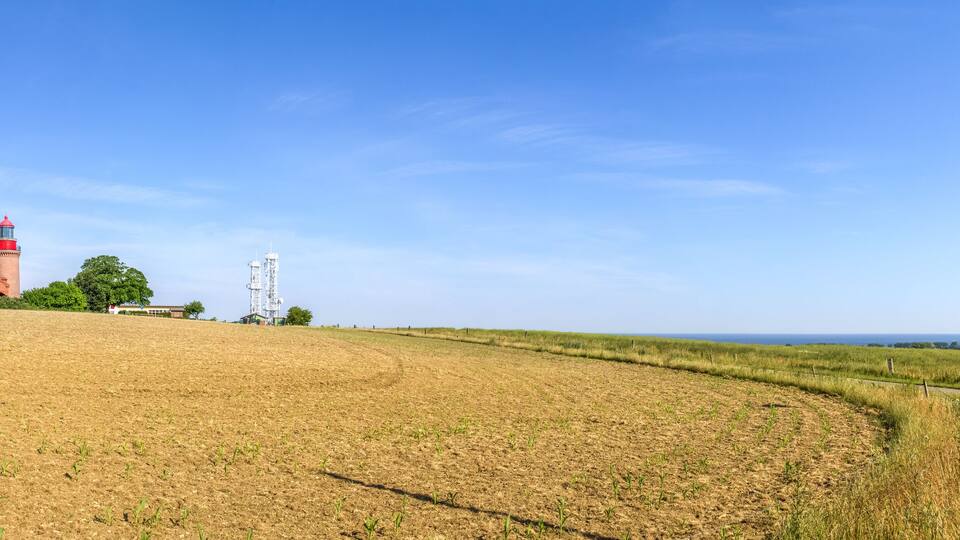 A coastal landscape with a lighthouse, a red-roofed building, and a clear blue sky.