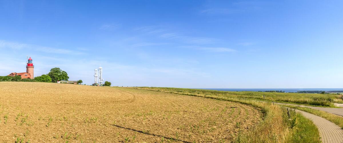 A coastal landscape with a lighthouse, a red-roofed building, and a clear blue sky.