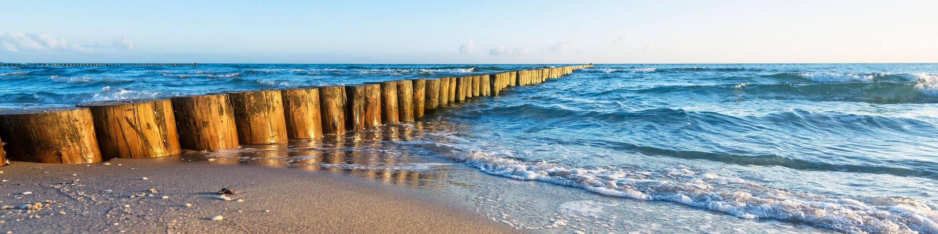 A wooden sea defense structure along a beach with waves crashing onto the shore.