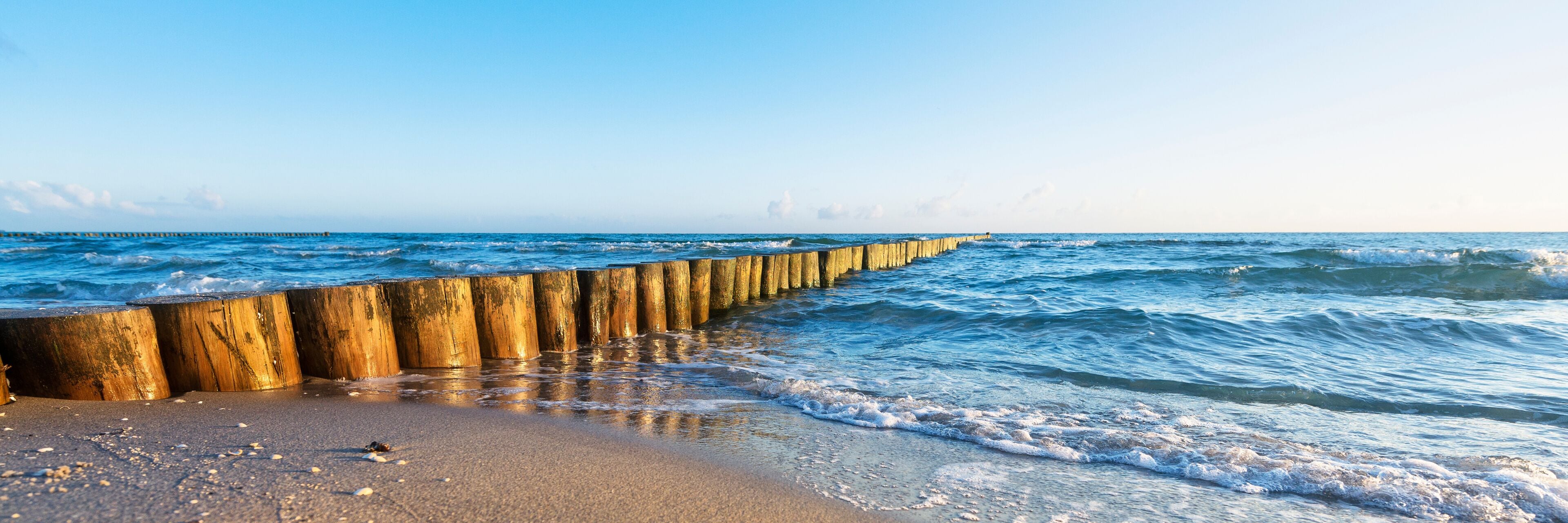 A wooden sea defense structure along a beach with waves crashing onto the shore.