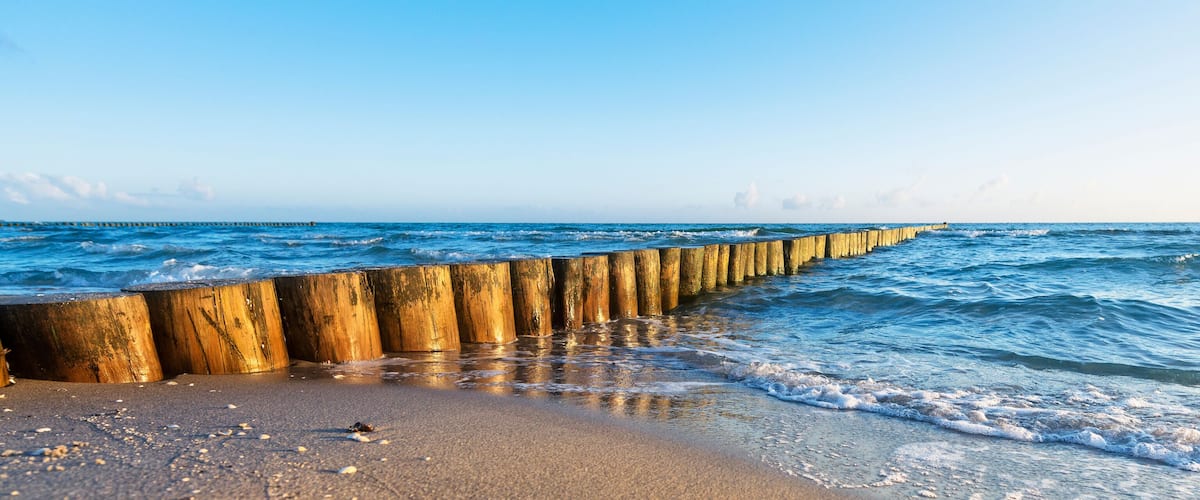 A wooden sea defense structure along a beach with waves crashing onto the shore.