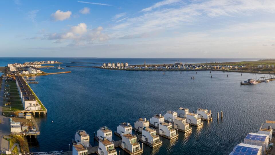 A coastal marina with floating houses and a long pier extending into the water.