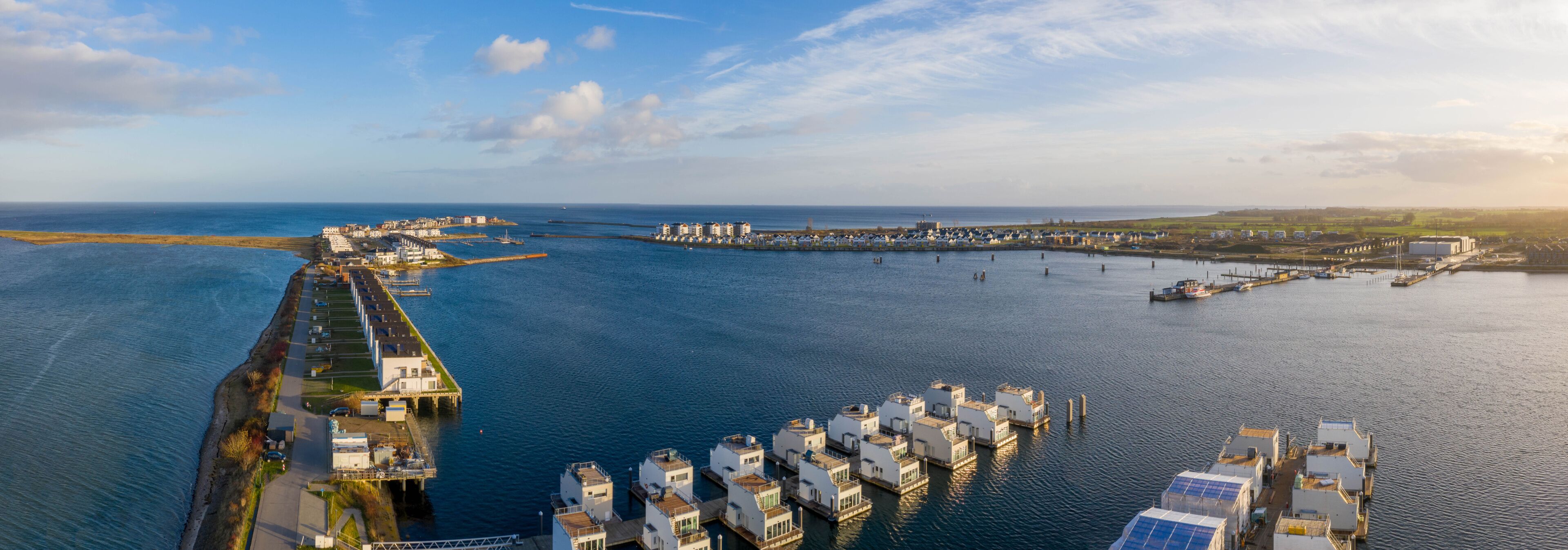 A coastal marina with floating houses and a long pier extending into the water.