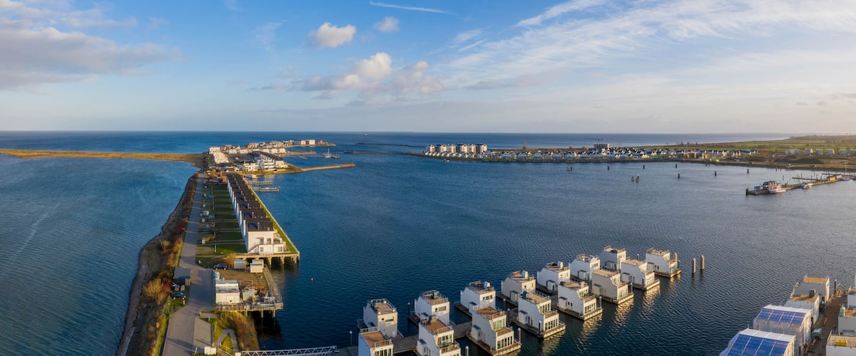 A coastal marina with floating houses and a long pier extending into the water.