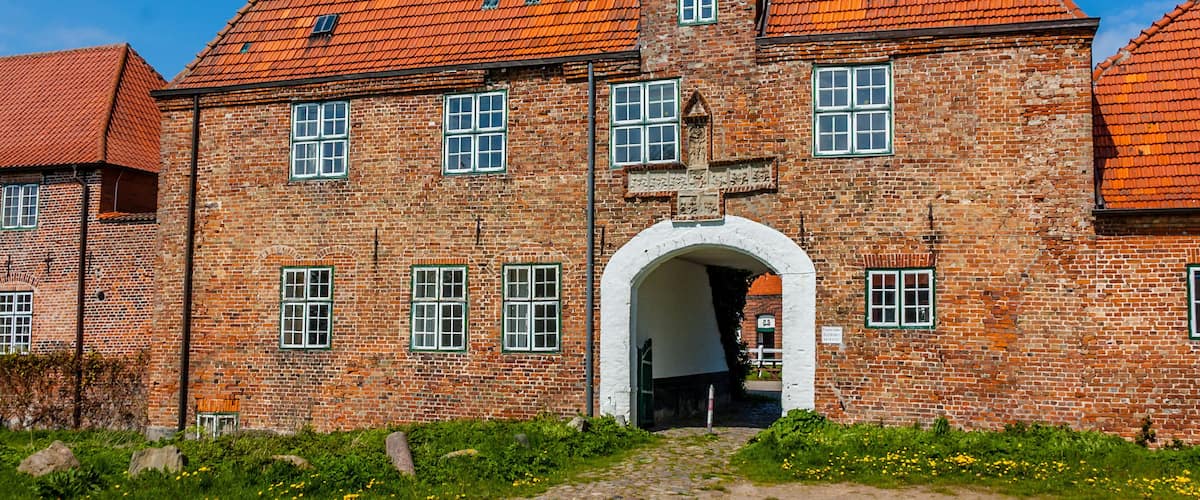 A historic brick building with a red-tiled roof and a prominent tower.