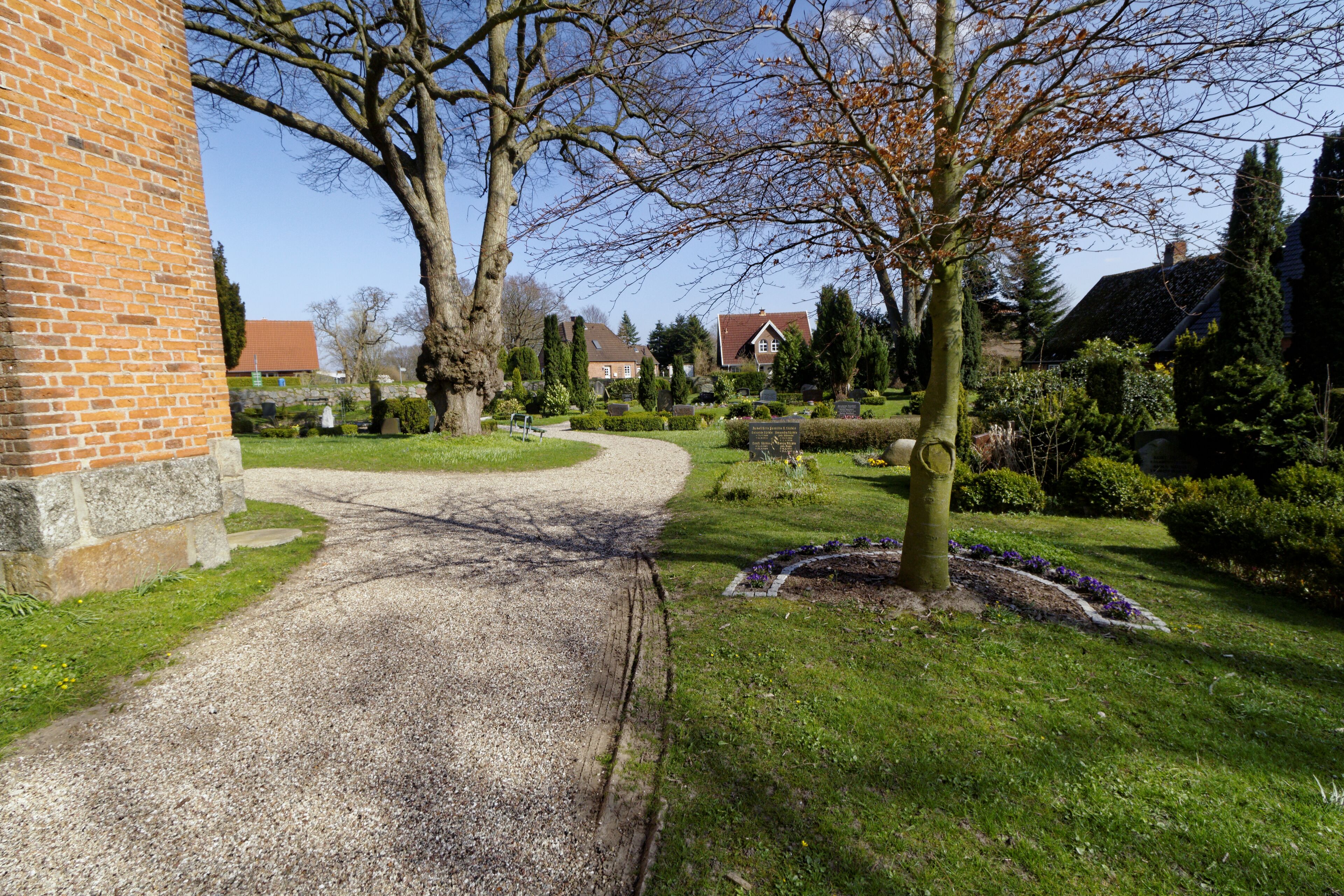A gravel path leading to a brick building, surrounded by trees and a well-maintained garden.