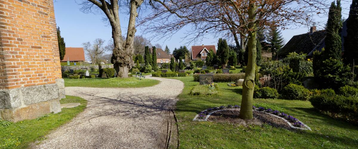 A gravel path leading to a brick building, surrounded by trees and a well-maintained garden.