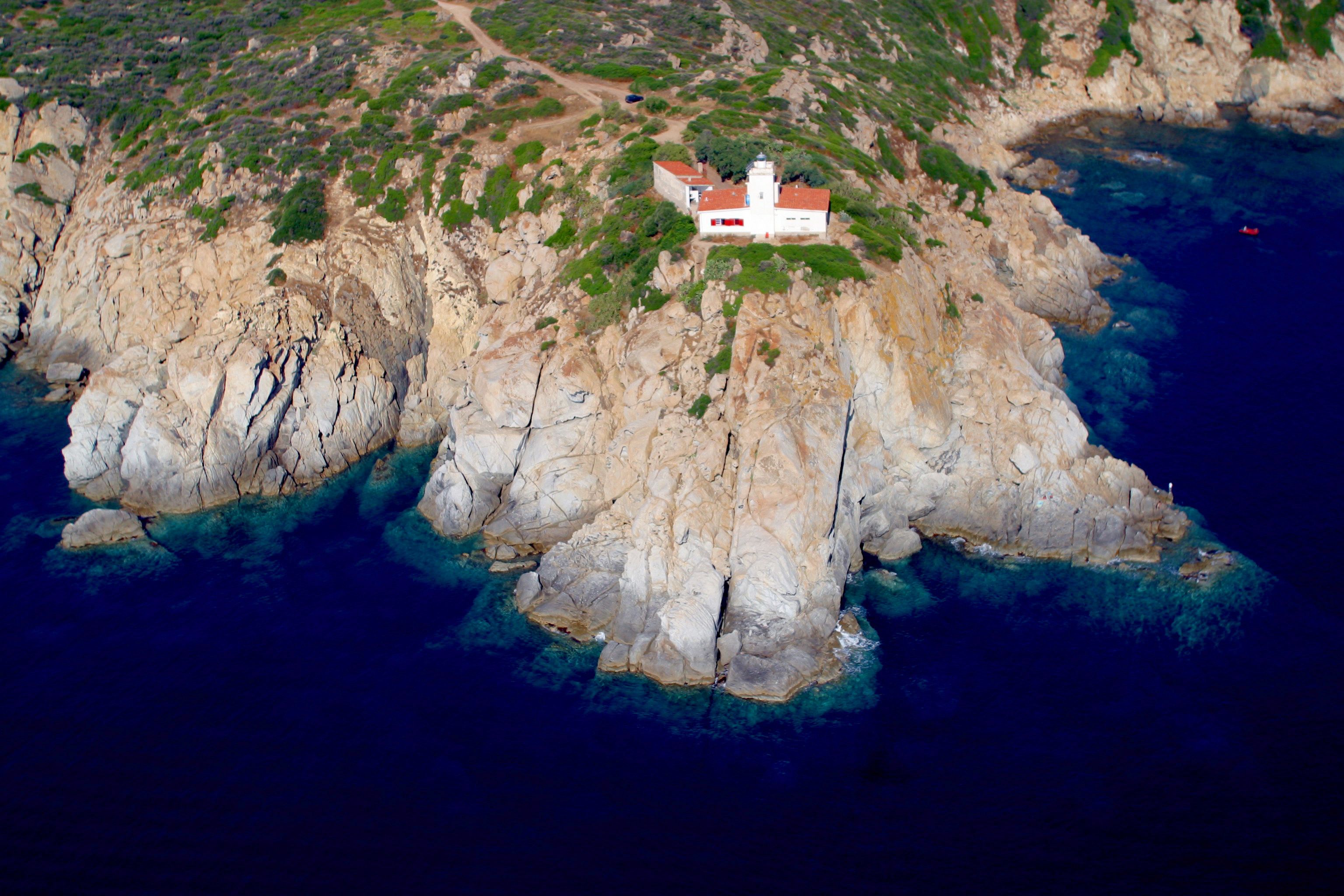 Paisagem costeira com um afloramento rochoso e um edifício branco com telhado vermelho.