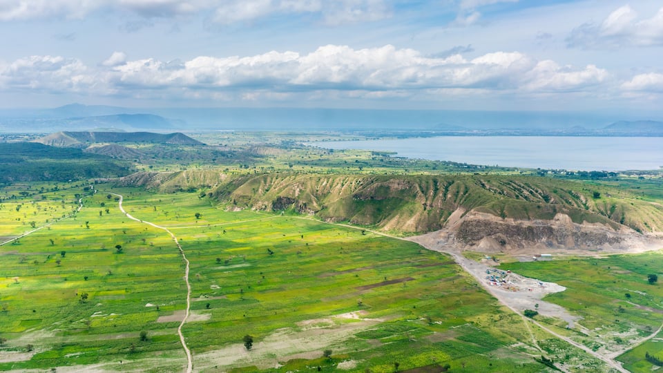 A vast green landscape with terraced fields, a winding road, and a distant body of water.