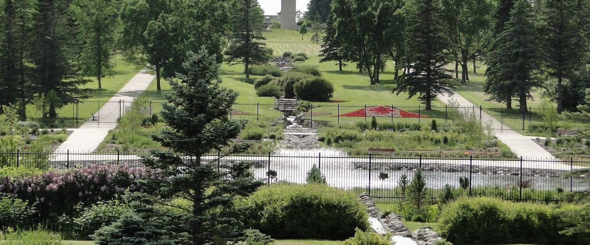 A park with two tall, dark towers, surrounded by trees and a pond.