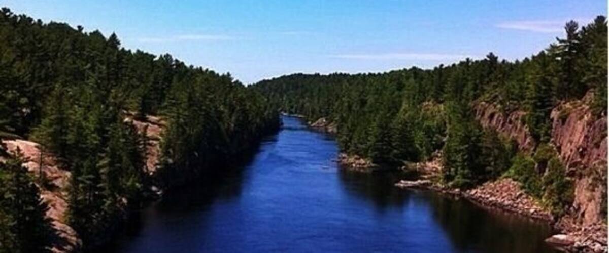 A river flanked by dense forests and rocky cliffs.